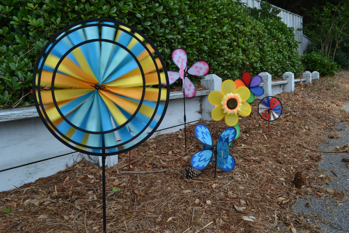 Multiple wind spinners in a sidewalk garden with green bushes behind