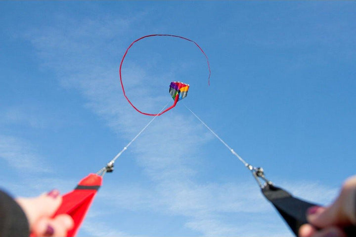 Hands holding two kite lines controlling a kite in the air
